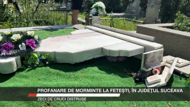 Mormânt vandalizat într-un cimitir, cu crucea spartă și flori împrăștiate pe jos.