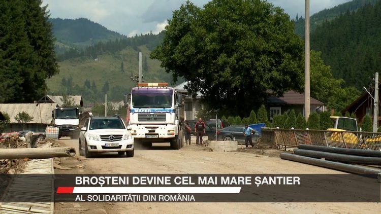 Imagine din Broșteni, cu utilaje și camioane pe un drum în lucru, în contextul reconstrucției după inundațiile din 2025.